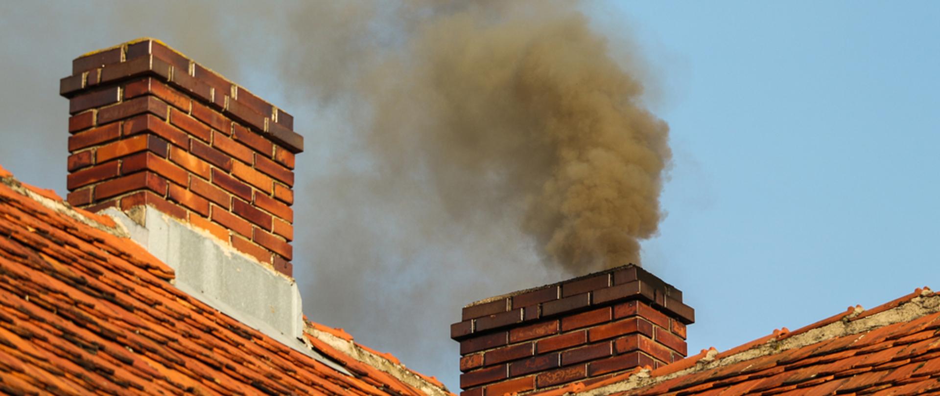 Czarny dym wylatujący z komina z czerwonej cegły stojącego na dachu pokrytym czerwoną dachówką