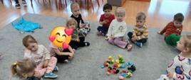 Grupa dzieci siedząca w kole. Na środku kolorowe kulki z papieru. W tle sylwety kolorowych potworów.