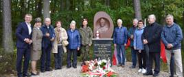 X Rajd Jubileuszowy imienia Zacheusza Nowowiejskiego w Górach Dębowych. Fotografia przedstawia organizatorów rajdu ustawionych po oby stronach pomnika upamiętniającego Zacheusza Nowowiejskiego: Nadleśnictwo Przasnysz, Rodzina Zacheusza Nowowiejskiego, Starostwo Powiatowe w Przasnyszu, Starostwo Powiatowe w Nidzicy. U podstawy pomnika umieszczono znicze oraz wiązanki kwiatów.