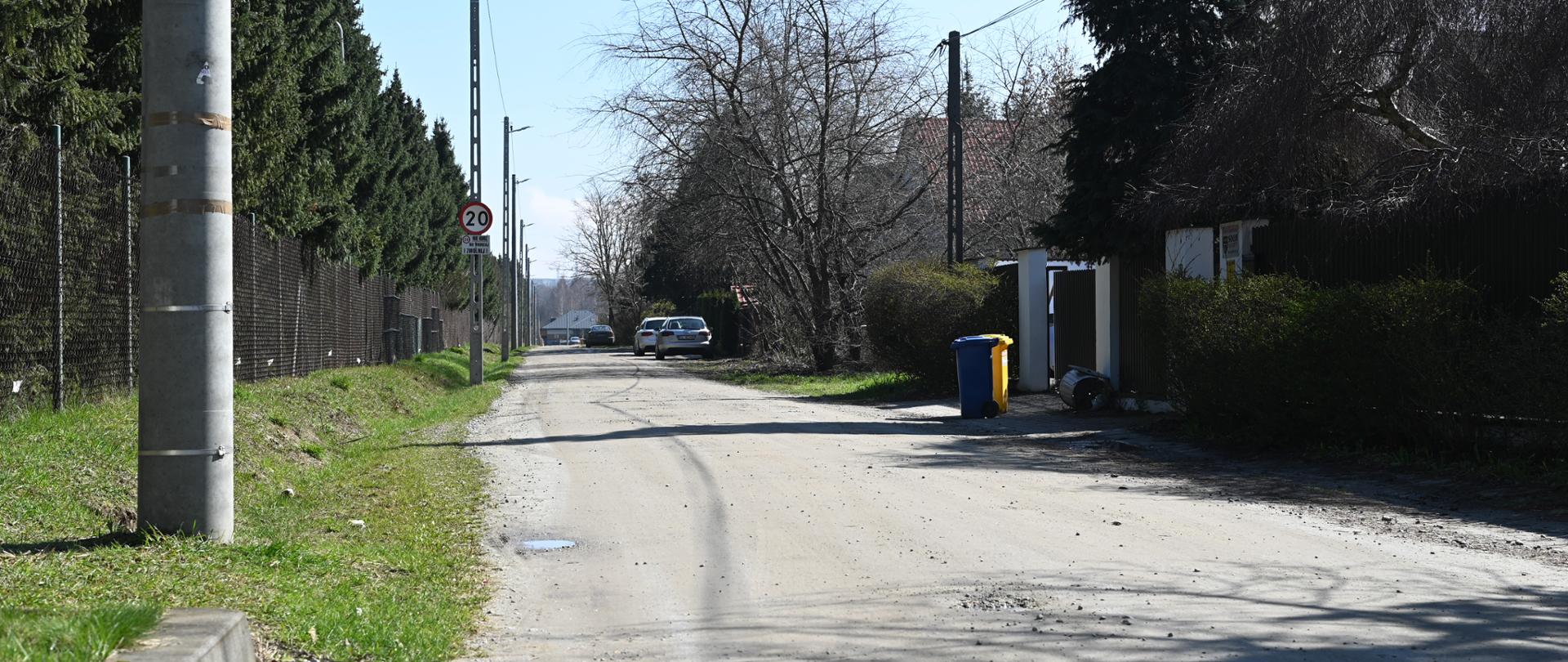 ulica Łanowa, niebieski i żółty kosz na śmieci, w oddali widać zaparkowane dwa samochody, pogoda słoneczna