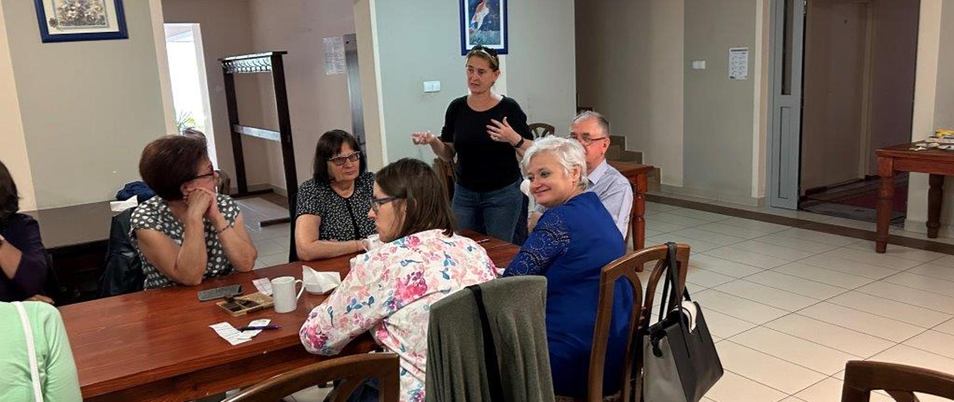 Podczas warsztatów kulinarnych - uczestnicy siedzą przy stole, słuchają trenerki