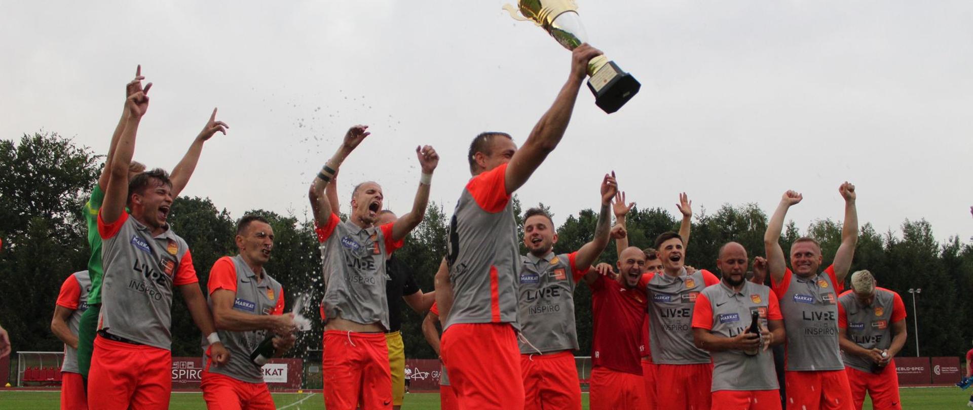 Zespół MKS Kalwarianka świętujący awans do IV ligi, grupa mężczyzn w strojach piłkarskich na pierwszym planie kapitan z pucharem. 
