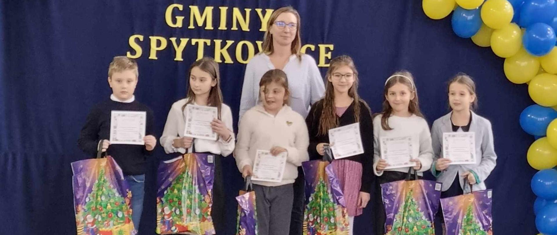 Uczniowie na tle dekoracji powieszonej na granatowym płótnie, w rękach trzymają dyplomy oraz nagrody otrzymane w Gminnym Konkursie Plastycznym "Stop Uzależnieniom.