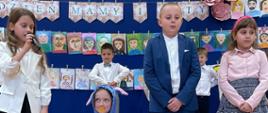 Uczniowie klas 1-3 odgrywają role mamy, taty oraz małego dziecka ze smoczkiem w buzi na przedstawieniu dla rodziców
