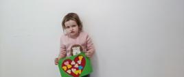 Dziewczynka pozuje do zdjęcia trzymając w ręku kartkę walentynkową