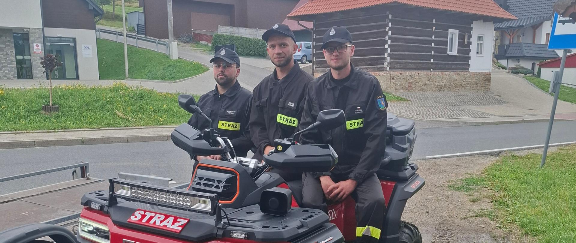 Mężczyźni siedzą na czerwonym qadzie. W tle widok na drogę.