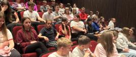 Uczniowie siedzą w fotelach w sali teatralnej