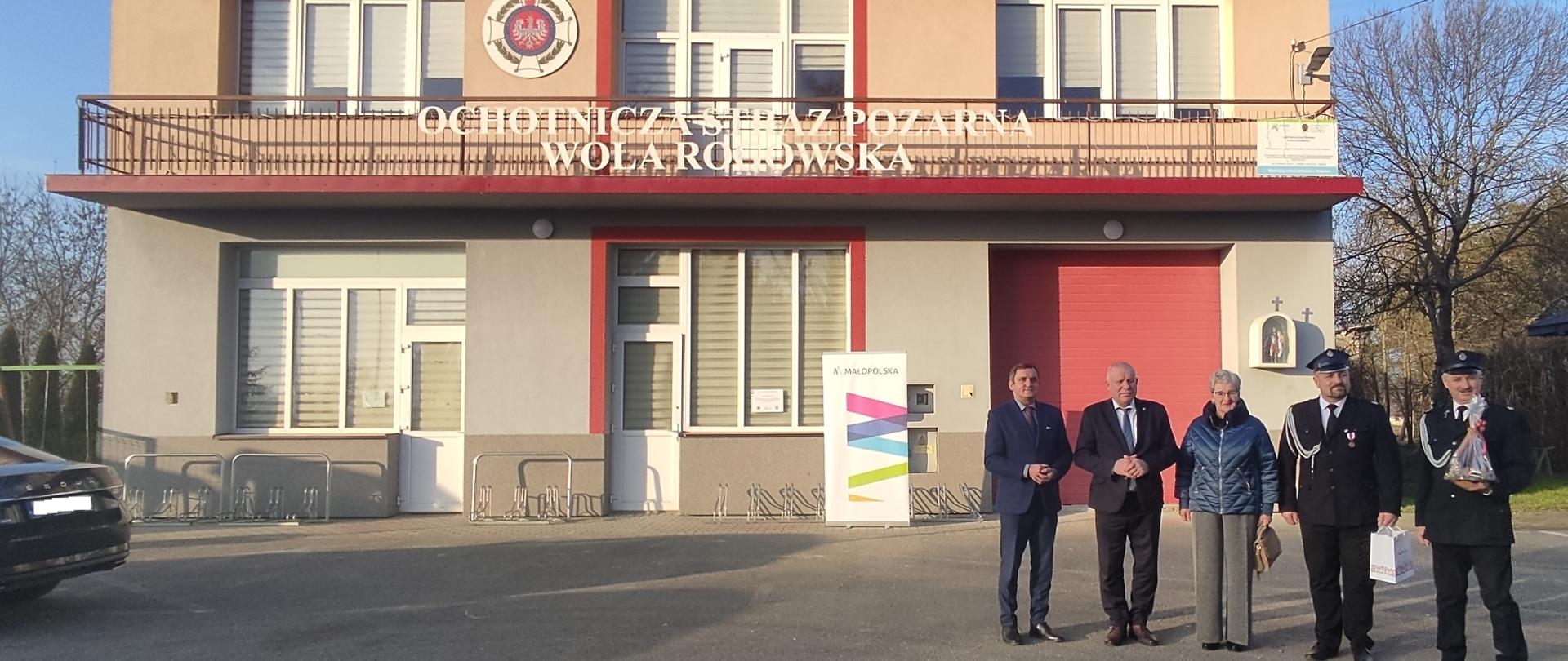 Budynek Ochotniczej Straży Pożarnej w Woli Radłowskiej z grupą osób stojących przed wejściem