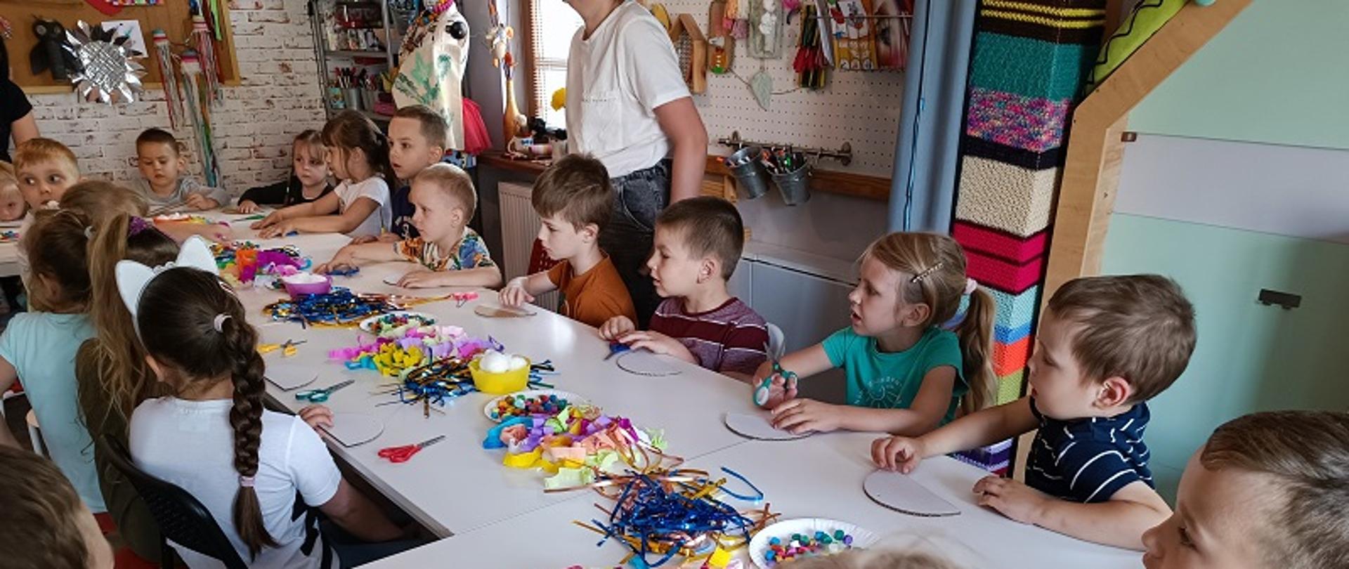 Dzieci siedzą przy stole, przed nimi elementy do tworzenia rękodzieła