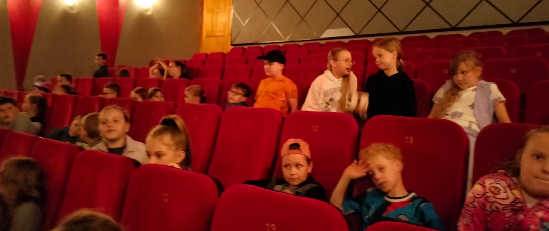 Na zdjęciu znajdują się dzieci siedzące na fotelach kinowych.