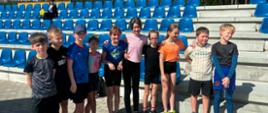 Na zdjęciu znajdują się reprezentanci naszej szkoły w zawodach lekkoatletycznych. Dziesięcioro uczniów naszej szkoły - pięć dziewczynek i pięcioro chłopców pozuje do wspólnego zdjęcia. Wszyscy ubrani są w stroje sportowe. Za nimi znajdują się trybuny.