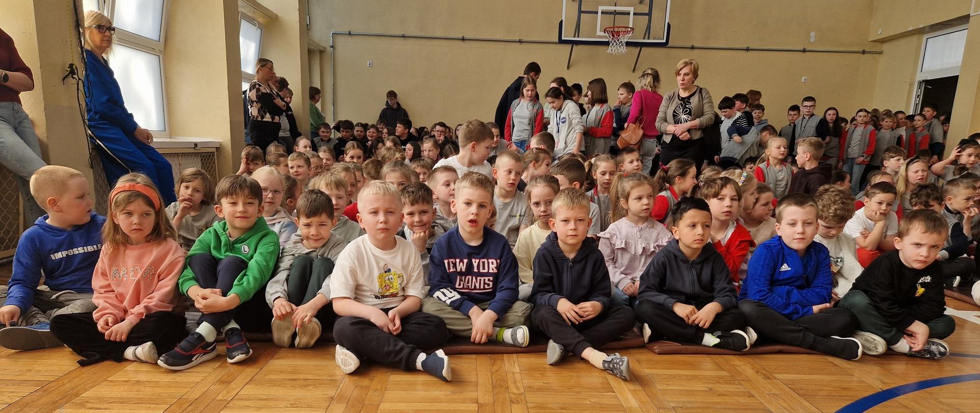 Grupa dzieci siedzi na sali gimnastycznej