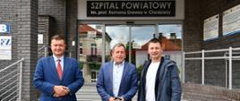 3 osoby stojące przed wejściem do budynku, nad wejściem napis Szpital Powiatowy im. prof. Romana Drewsa w Chodzieży