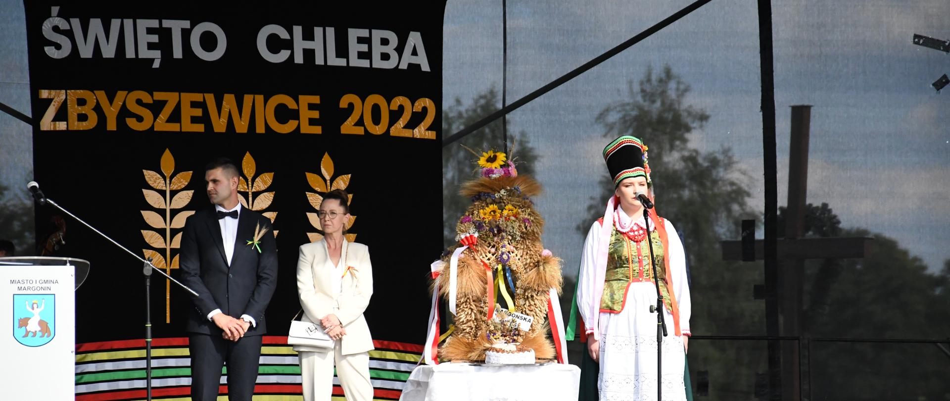 3 osoby i wieniec dożynkowy na scenie, w tle napis Święto chleba Zbyszewic 2022