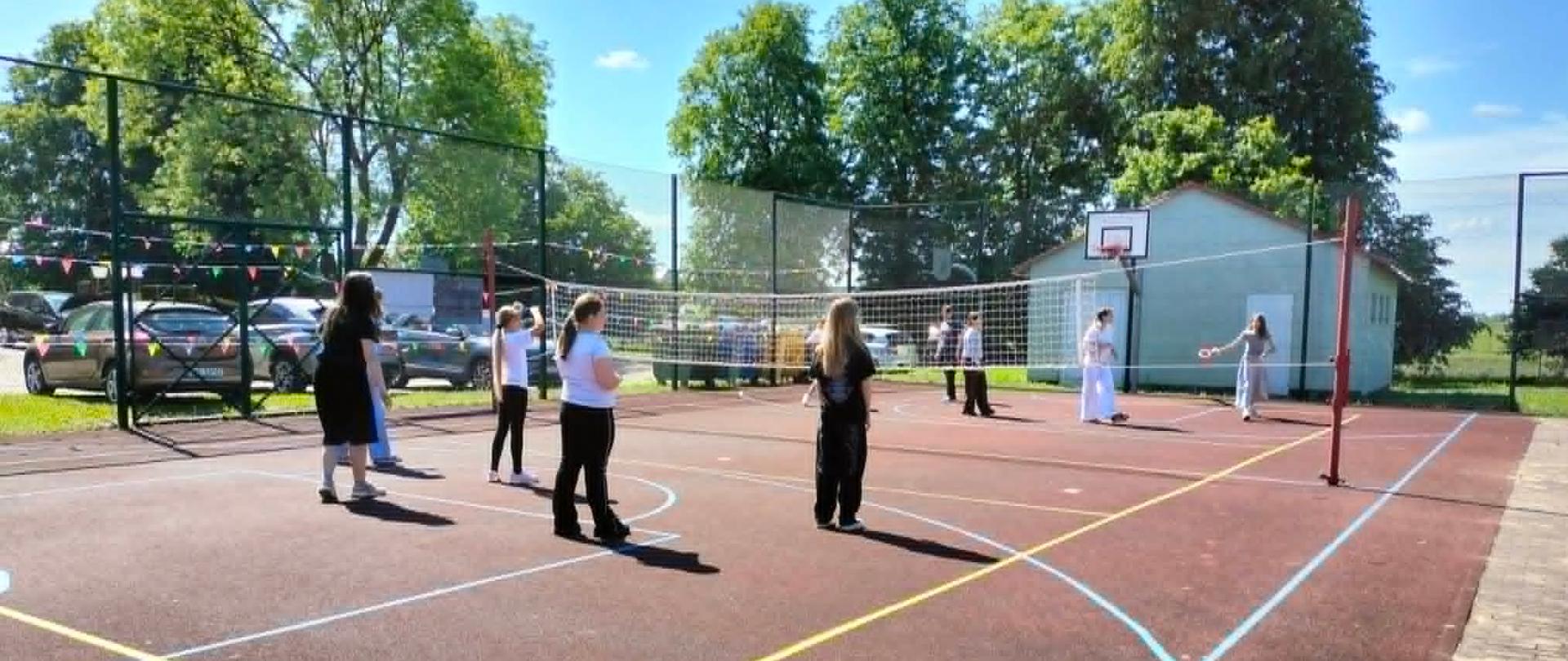 Uczennice klas starszych stoją na boisku do siatkówki i rzucają do siebie krążkiem ringo.