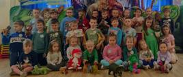 Wspólne zdjęcie wszystkich przedszkolaków na tle dekoracji przedstawiającej dinozaury.