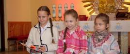 Trzy uczennice stoją przy ołtarzu, trzymają w rękach dyplomy i nagrody