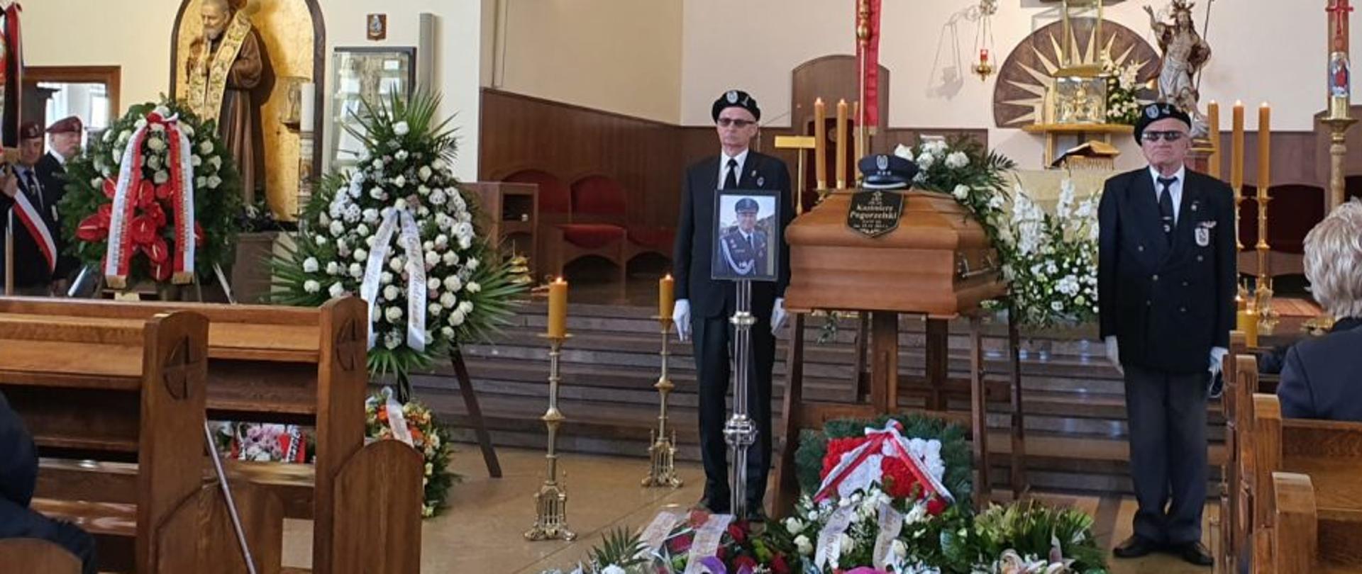 Wnętrze kościoła, na środku trumna obok której stoi dwóch mężczyzn przed nią wieńce.