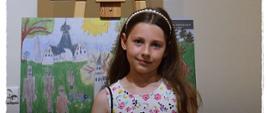 Uczestniczka konkursu pozuje przy pracach plastycznych