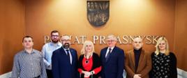 Zdjęcie przedstawia przedstawicieli Mazowieckiej Izby Gospodarczej wizytujących w Starostwie Powiatowym w Przasnyszu. Od lewej: Kierownik Referatu Promocji Marek Chrzanowski, Starszy Inspektor ds. Promocji, Starosta Przasnyski Krzysztof Bieńkowski, troje przedstawicieli Mazowieckiej Izby Gospodarczej oraz pracownik Referatu Magdalena Kowalewska. Za nimi na ścianie duży złoty napis Powiat Przasnyski, a nad napisem przedstawienie herbu Powiatu Przasnyskiego.