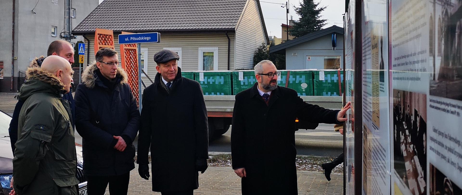 Zdjęcie wykonane w Przasnyszu przy Szkole Podstawowej Nr 2 imienia Henryka Sienkiewicza. Fotografia przedstawia Starostę Przasnyskiego Krzysztofa Bieńkowskiego prezentującego wystawę umieszczoną na ogrodzenia szkolnego boiska. Wystawa składa się z wielkoformatowych plansz, na których umieszczono historię polskiego urzędu prezesa rady ministrów pod tytułem „Od Moraczewskiego do Morawieckiego. Premierzy Rzeczypospolitej Niepodległej 1918-2018". Na zdjęciu od lewej: Dyrektor Szkoły Podstawowej Nr 2 w Przasnyszu Piotr Jeronim, Burmistrz Przasnysza Łukasz Chrostowski, Kierownik Delegatury Mazowieckiego Urzędu Wojewódzkiego w Ostrołęce Marcin Grabowski, Wojewoda Mazowiecki Konstanty Radziwiłł, Starosta Przasnyski Krzysztof Bieńkowski.
