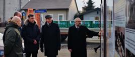 Zdjęcie wykonane w Przasnyszu przy Szkole Podstawowej Nr 2 imienia Henryka Sienkiewicza. Fotografia przedstawia Starostę Przasnyskiego Krzysztofa Bieńkowskiego prezentującego wystawę umieszczoną na ogrodzenia szkolnego boiska. Wystawa składa się z wielkoformatowych plansz, na których umieszczono historię polskiego urzędu prezesa rady ministrów pod tytułem „Od Moraczewskiego do Morawieckiego. Premierzy Rzeczypospolitej Niepodległej 1918-2018". Na zdjęciu od lewej: Dyrektor Szkoły Podstawowej Nr 2 w Przasnyszu Piotr Jeronim, Burmistrz Przasnysza Łukasz Chrostowski, Kierownik Delegatury Mazowieckiego Urzędu Wojewódzkiego w Ostrołęce Marcin Grabowski, Wojewoda Mazowiecki Konstanty Radziwiłł, Starosta Przasnyski Krzysztof Bieńkowski.