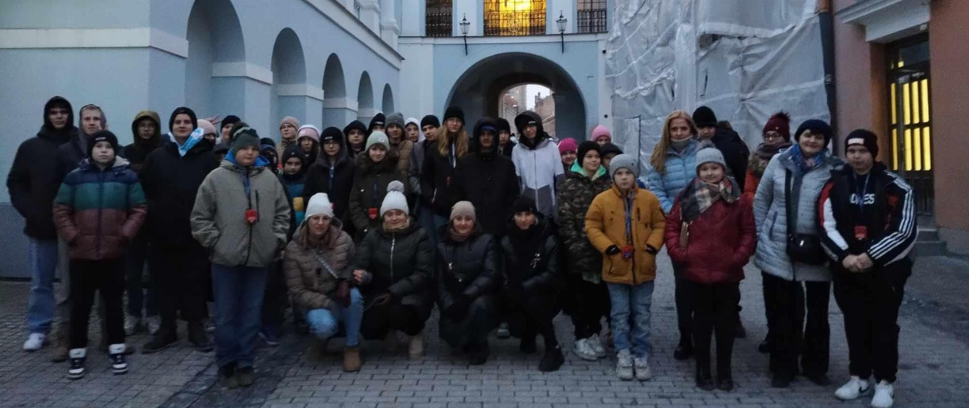 Grupa młodzieży wraz z nauczycielami pozuje na tle Ostrej Bramy w Wilnie.