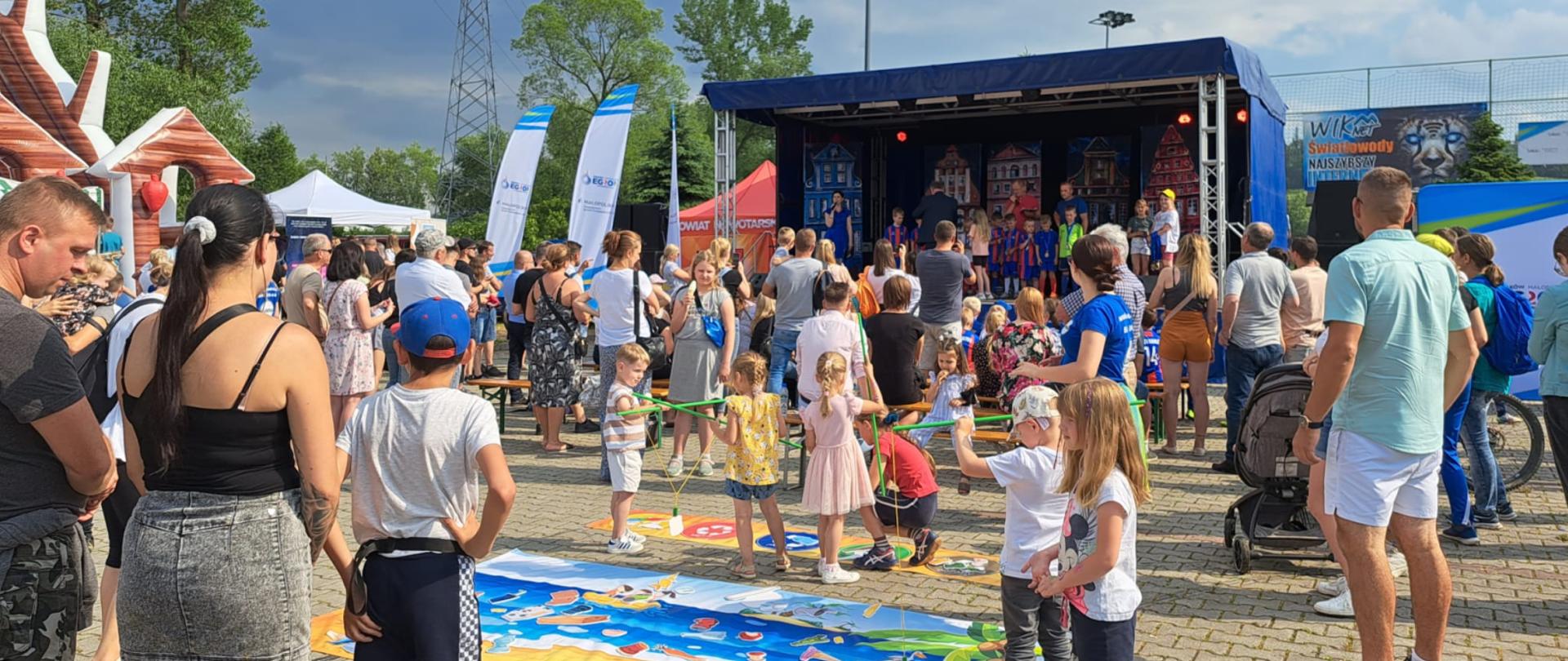 Zdjęcie przedstawia ludzi zebranych przed sceną oraz bawiące się dzieci