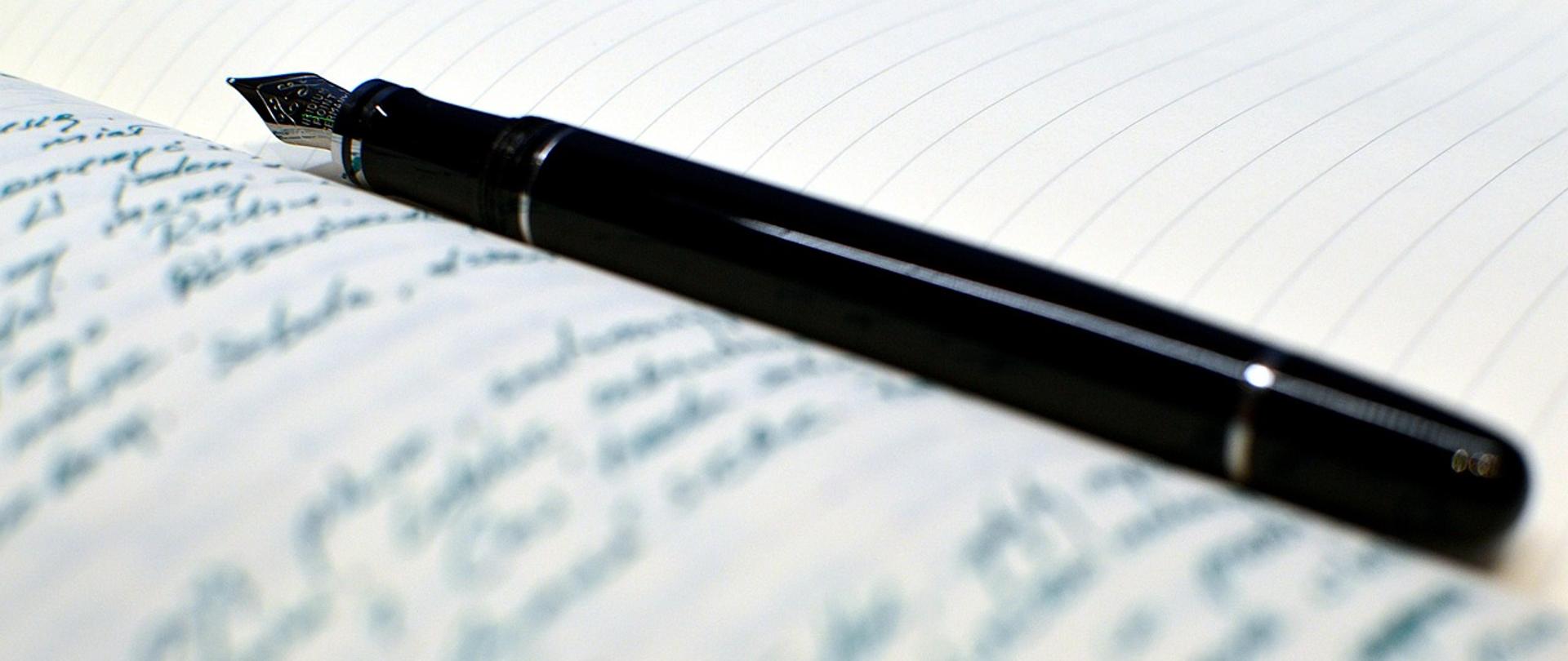 Zdjęcie przedstawia pióro do pisania położone na zapisanej kartce papieru