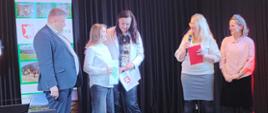 Nagrodzona uczennica trzyma w ręku nagrodę oraz dyplom, pozuje do zdjęcia z panią wójt i wicewójtem, obok stoją 2 panie organizatorki konkursu