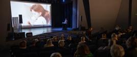 Uczestnicy konferencji w Centrum Kultury i Wypoczynku w Proszowicach podczas spotkania, na scenie jeden z prelegentów
