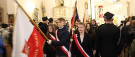 Młodzież wychodzi z kościoła. Chłopcy niosą w rękach uniesione sztandary. Przepasani są biało czerwonymi wstążkami