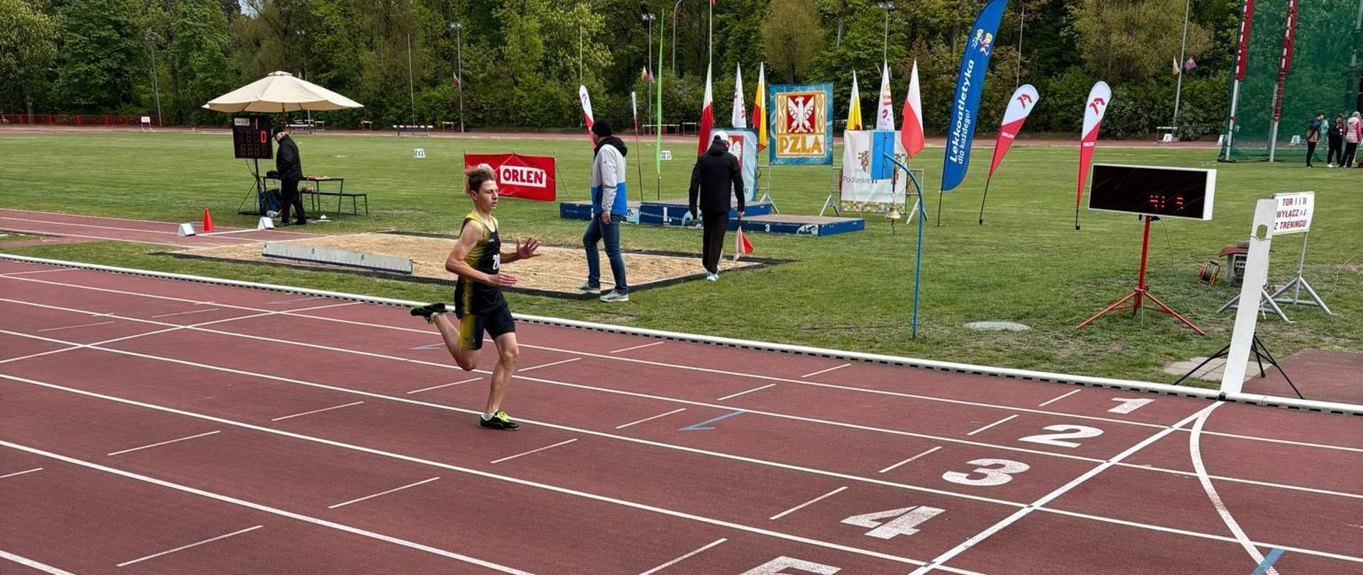 Chłopak ubrany w strój sportowy biegnie po stadionie lekkoatletycznym.
