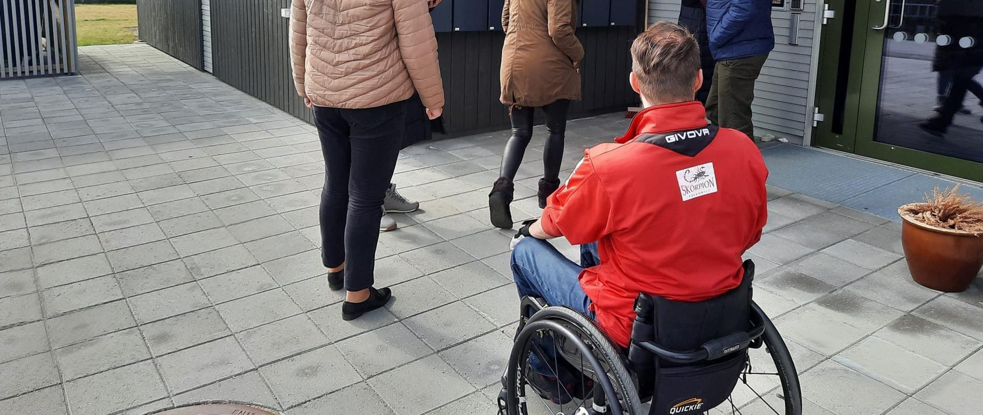 Mężczyzna na wózku inwalidzkim i grupa ludzi wchodzą do budynku