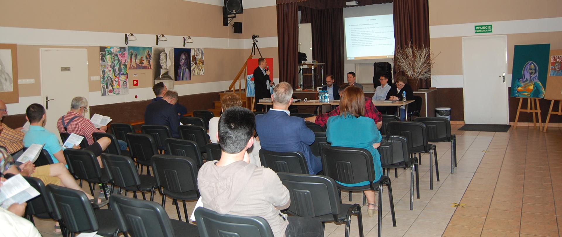 Spotkanie organizacyjne - prezentacja multimedialna referowana przez mężczyznę mówiącego do mikrofonu przy udziale kilkunastu osób w sali GOK w Nakle Śląskim