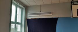 Sala OSP w Turzynie z zainstalowaną kurtyną powietrzną pod sufitem. Po lewej stronie znajduje się okno zabezpieczone siatką.