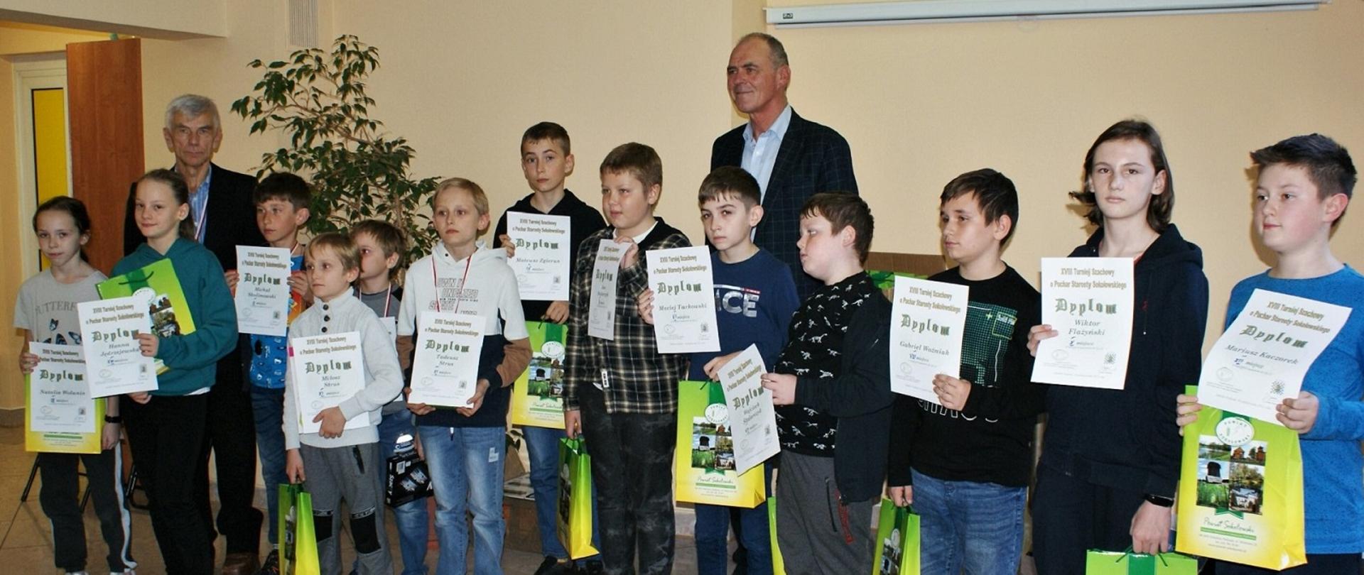 Na zdjęciu grupowym uczestnicy Turnieju w kategorii juniorzy do lat 12, którzy trzymają w dłoniach dyplomy oraz torby z nagrodami ufundowanymi przez Powiat Sokołowski. Wraz z dziećmi na zdjęciu widzimy organizatora pana Józefa Flazińskiego reprezentującego STSz oraz wicestarostę Ryszarda Domańskiego, który wręczył laureatom nagrody.