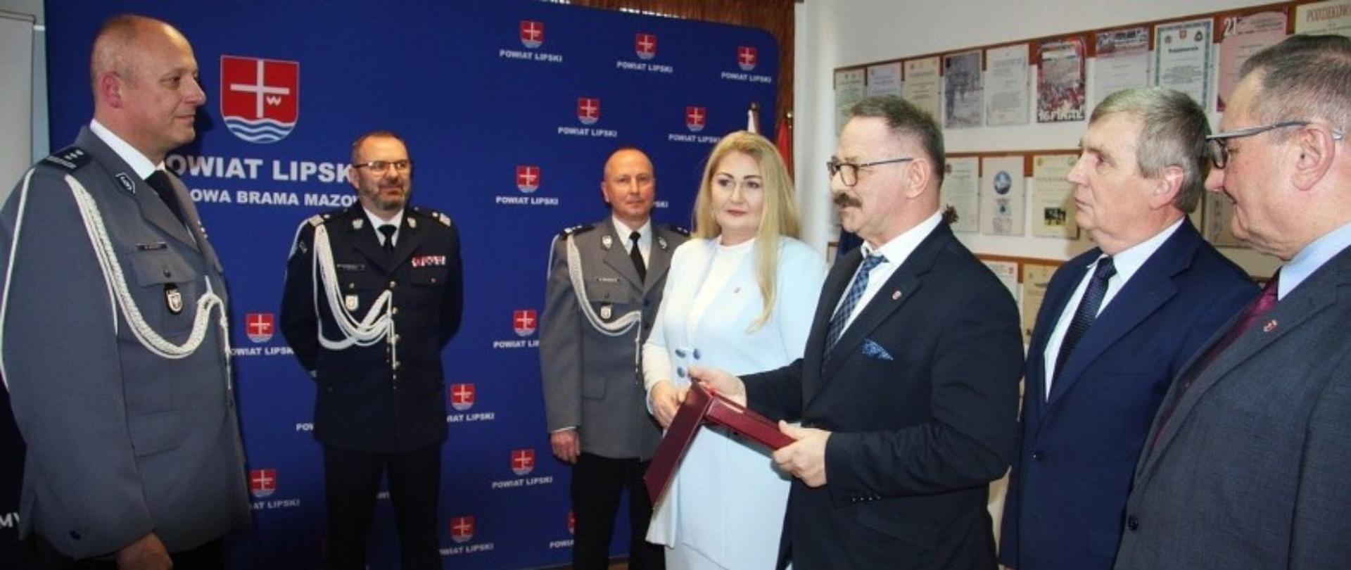 Przedstawiciele Powiatu Lipskiego wręczają inspektorowi Wojciechowi Brandtowi pamiątkowy grawerton.