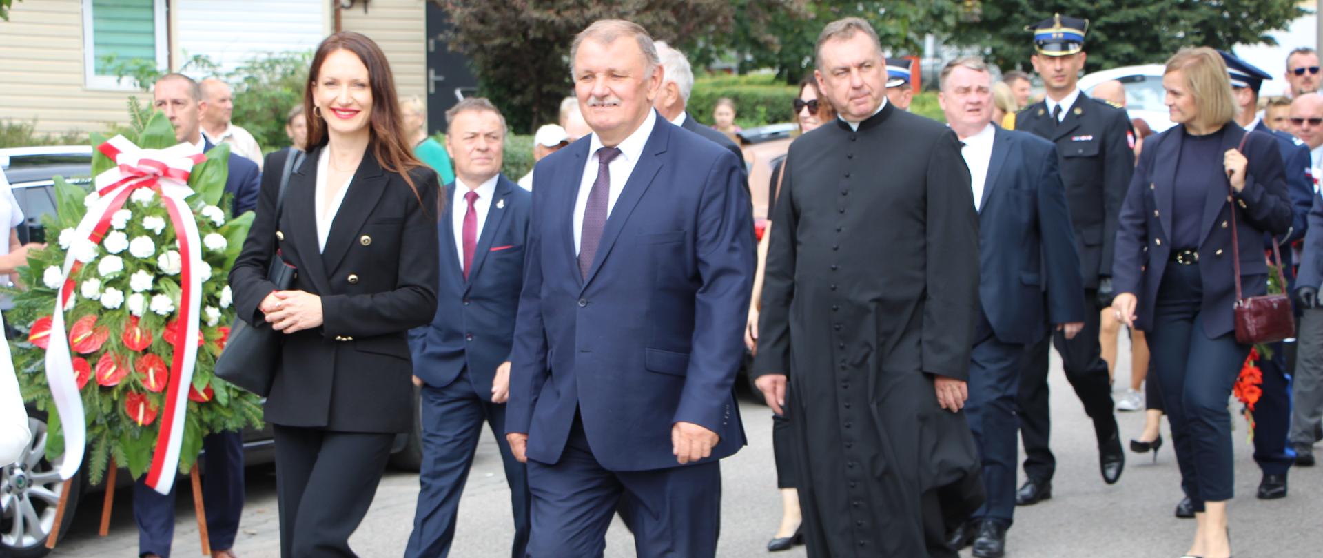 na zdjęciu znajdują się: starosta zambrowski i członek zarządu powiatu zambrowskiego, w tle przemarsz zaproszonych gości
