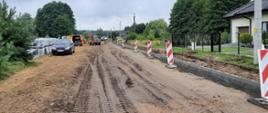 Rozbudowywany odcinek drogi. Zerwany asfalt, obsadzone krawężniki, w tle koparki, wywrotki oraz inne samochody.