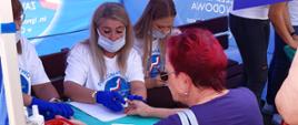 Festyn Profilaktyczno Zdrowotny w ogrodach przasnyskiego szpitala. Na zdjęciu przedstawiono uczestniczkę Festynu w trakcie badania poziomu cukru we krwi przez obsługę stanowiska Państwowej Szkoły Zawodowej imienia Ignacego Mościckiego w Ciechanowie.