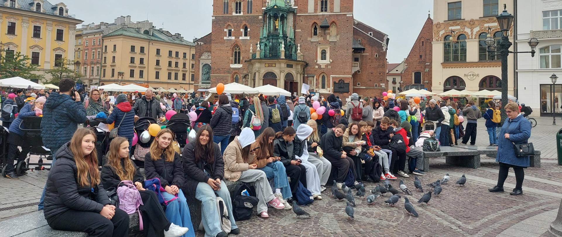 Uczniowie siedzą na Rynku Głównym w Krakowie.