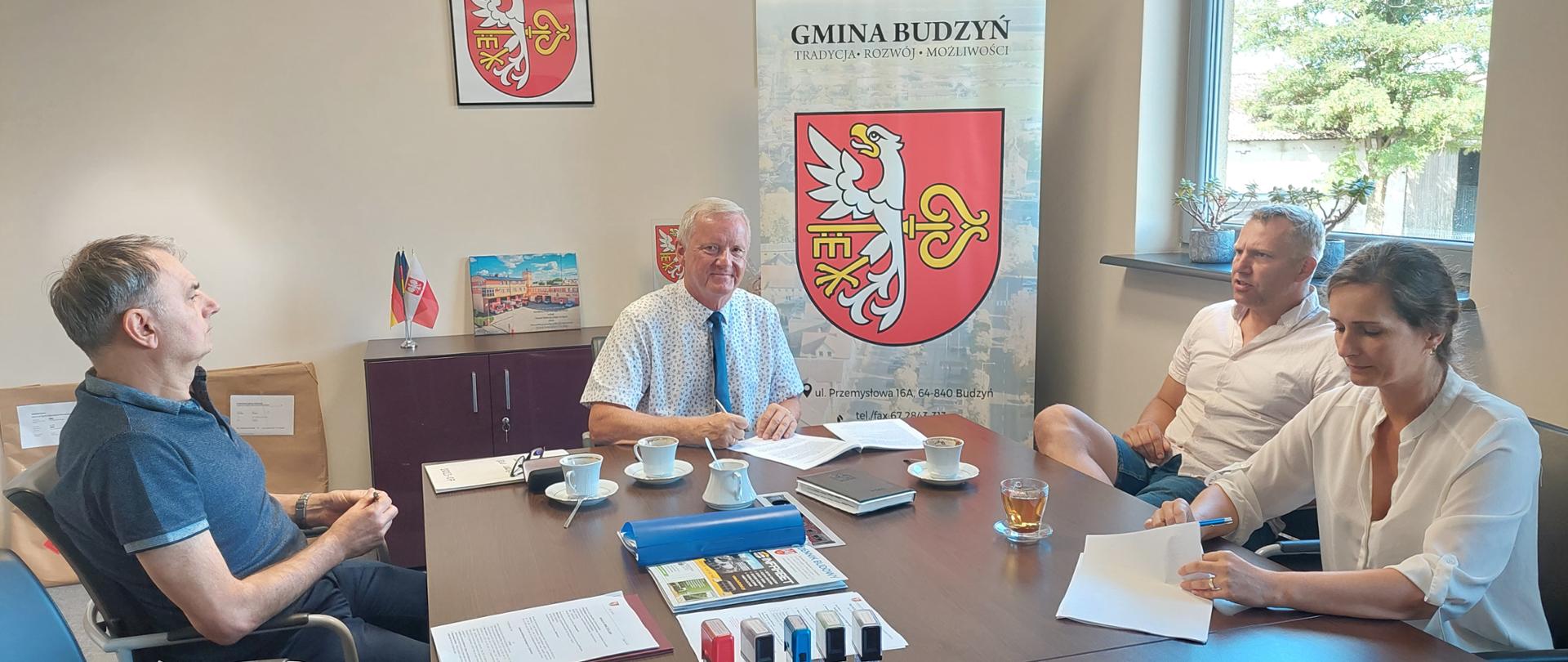 Cztery osoby siedzące przy stole, przed nimi dokumenty do podpisu