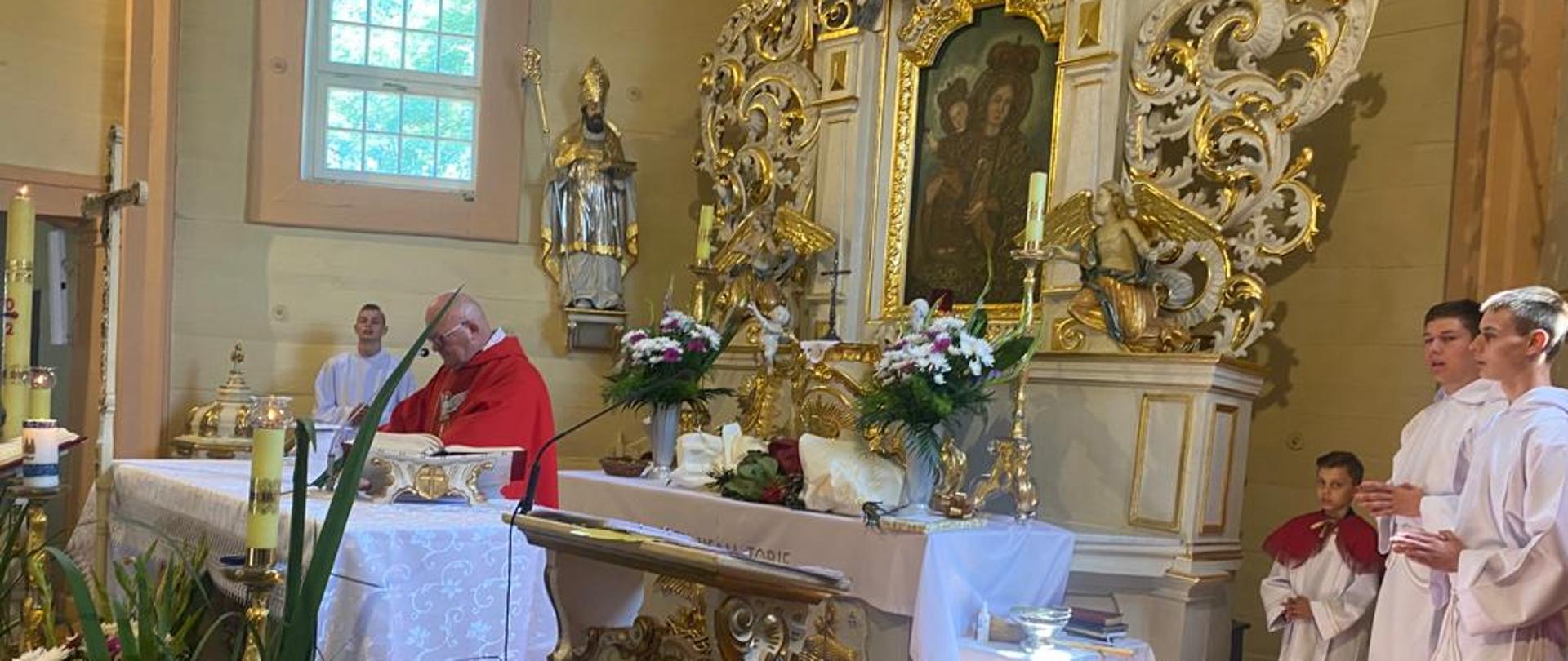 ołtarz kościoła w Żoniu z dużą ilością białych i złotych elementów, po bokach i przed ołtarzem stoją postacie