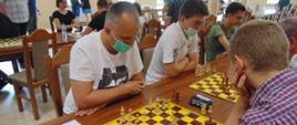 Grupa osób siedzi przy stołach, na stołach plansze do gry w szachy