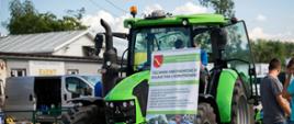 Na pierwszym planie zielony ciągnik rolniczy, przy nim roll- up Zespołu Szkół w Piotrkowicach Małych promujący kierunek kształcenia w zawodzie technik mechanizacji rolnictwa i agrotroniki.