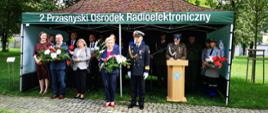 Zdjęcie wykonano w Parku Miejskim przy ulicy Makowskiej w Przasnyszu. Na fotografii przedstawiciele delegacji przybyłych na przasnyskie obchody wybuchu II Wojny Światowej. Od lewej Przewodnicząca Rady Powiatu Przasnyskiego Katarzyna Wróblewska, Wiceburmistrz Przasnysza Łukasz Machałowski, Wicestarosta Jarosław Szmulski, Sekretrz Gminy Przasnysz Bożena Rudzińska, Dyrektor Zespołu Szkół Powiatowych w Przasnyszu Paweł Szczepkowski, Poseł Anna Cicholska, Wiceprzewodniczący Rady Gminy Przasnysz Robert Kacprzak, przedstawiciel służb mundurowych. W głębi namiotu pozostali przedstawiciele służb mundurowych.