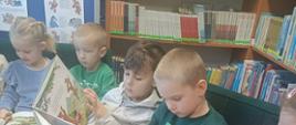 Przedszkolaki siedzą na kanapie w bibliotece i oglądają książeczki, z tyłu regały z książkami