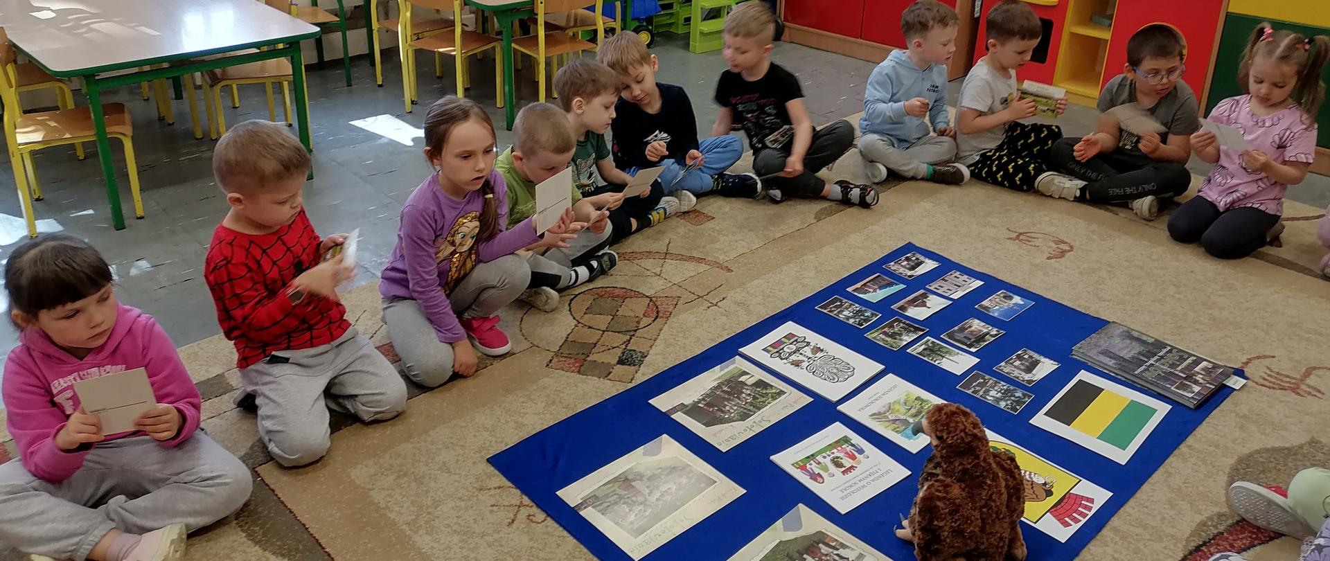 Grupa dzieci siedzi na dywanie- na dywanie zdjęcia i, herb i flaga Sokołowa 