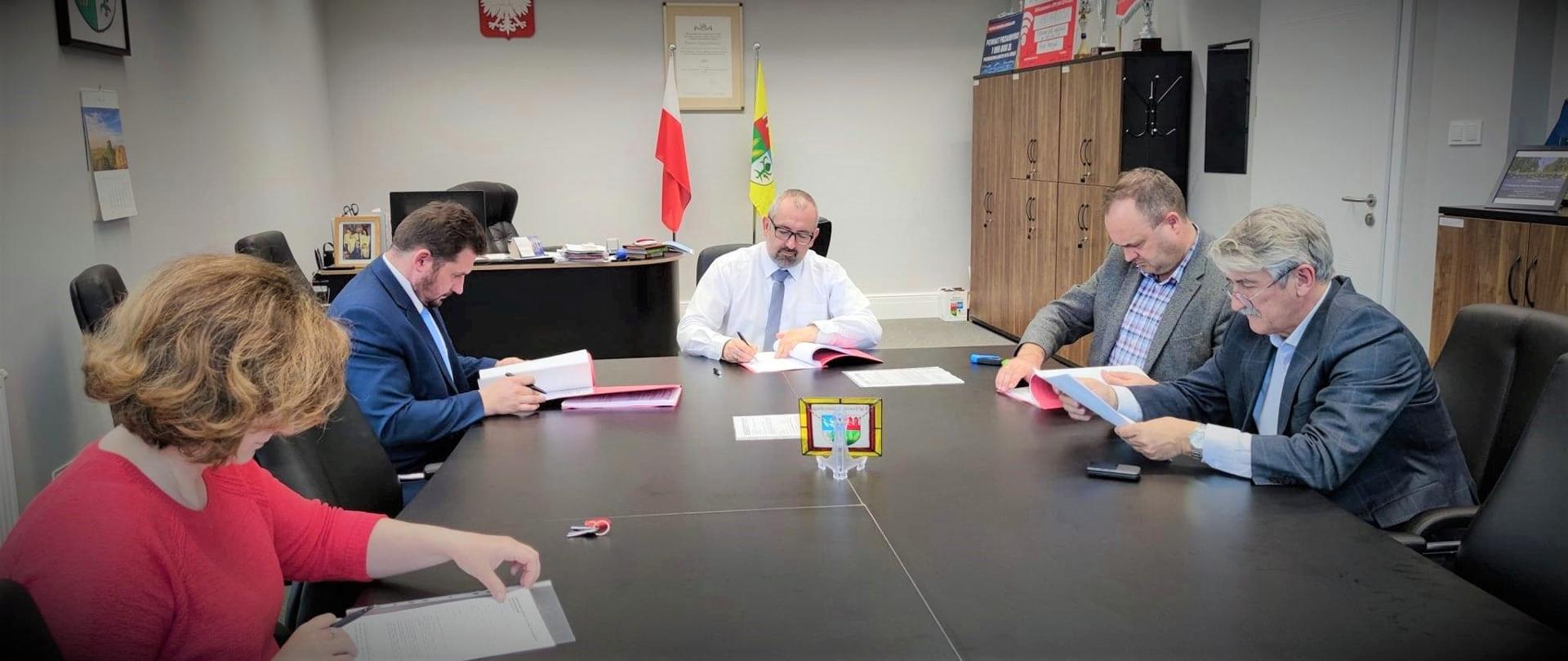 Zdjęcie przedstawia podpisanie umowy na wykonanie przebudowy drogi wojewódzkiej 614. Od prawej Skarbnik Powiatu Przasnyskiego Beata Czaplicka, Etatowy Członek Zarządu Paweł Mostowy, Starosta Przasnyski Krzysztof Bieńkowski, przedstawiciel przedsiębiorstwa "Ostrada" Sp. z o.o., Dyrektor Powiatowego Zarządu Dróg Kazimierz Pióro.